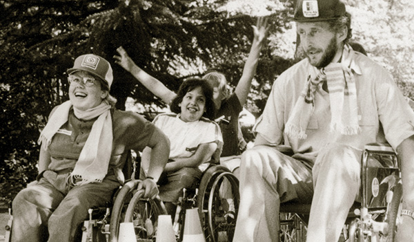 Schwarzweiss Archivfoto, Kinder und ein erwachsener bei einer geschicklichkeits hinterniss- Fahrt in Rollstühlen.